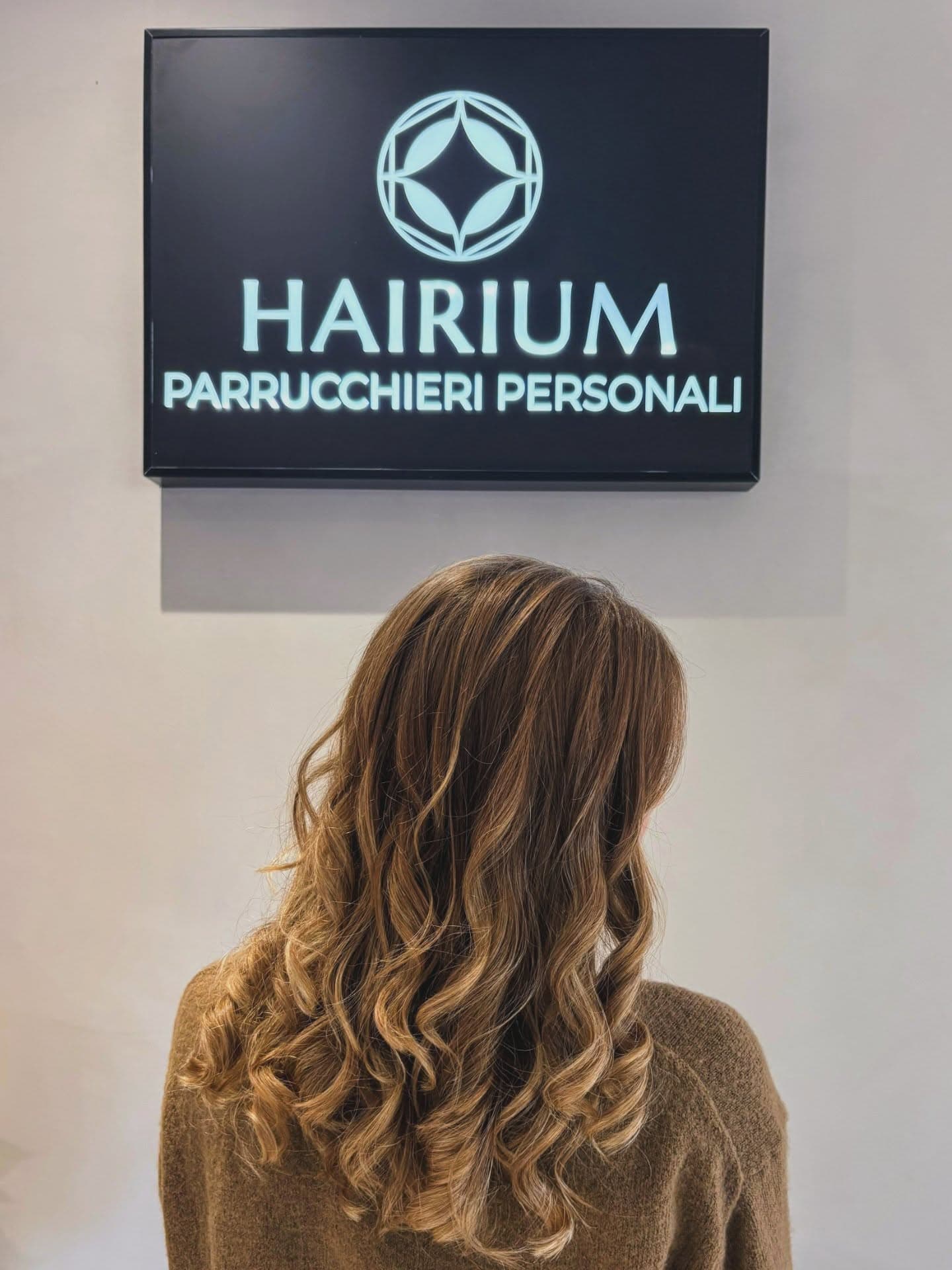 Capelli castani mossi visti da dietro sotto l'insegna Hairium Parrucchieri Personali