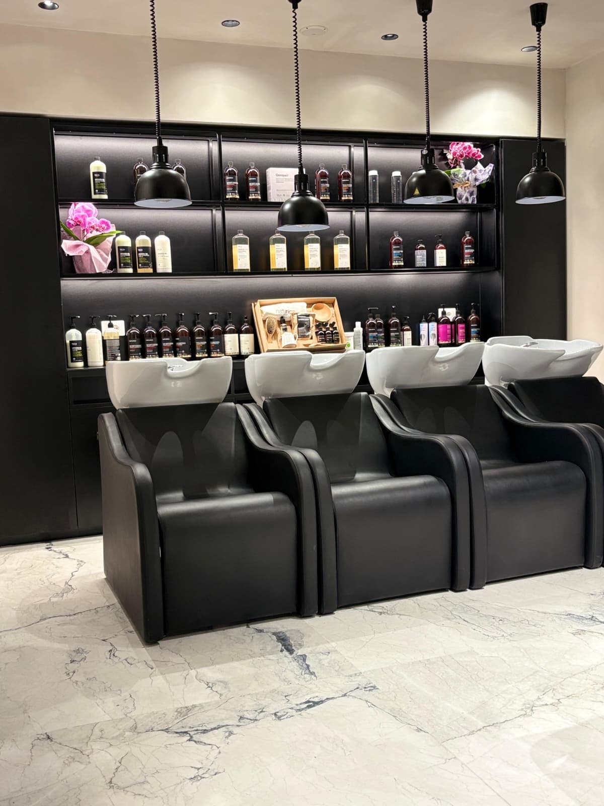 L'area lavaggio del salone Hairium con poltrone nere, luci soffuse e scaffali illuminati
