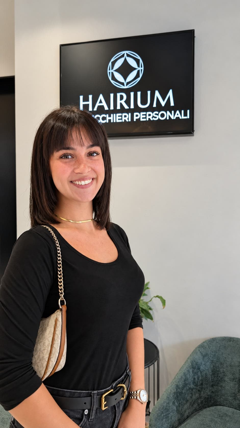 Una cliente sorride sotto l'insegna Hairium Parrucchieri Personali, con un caschetto scuro e la frangia